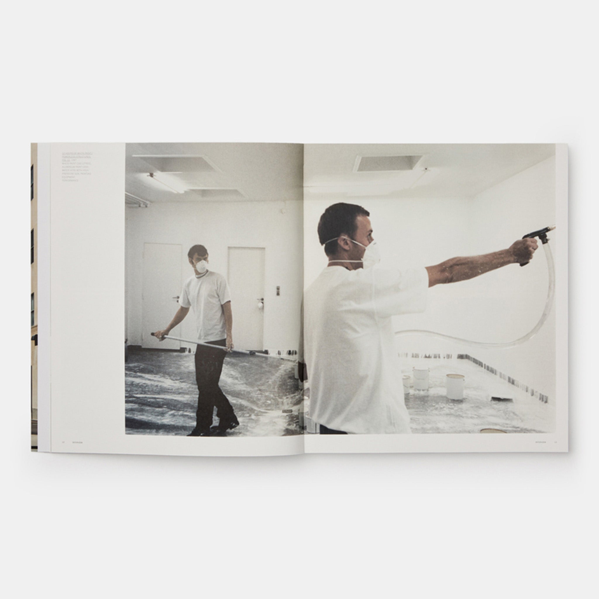The book is open to two pages and has a photograph of the artists creating a work across both pages.