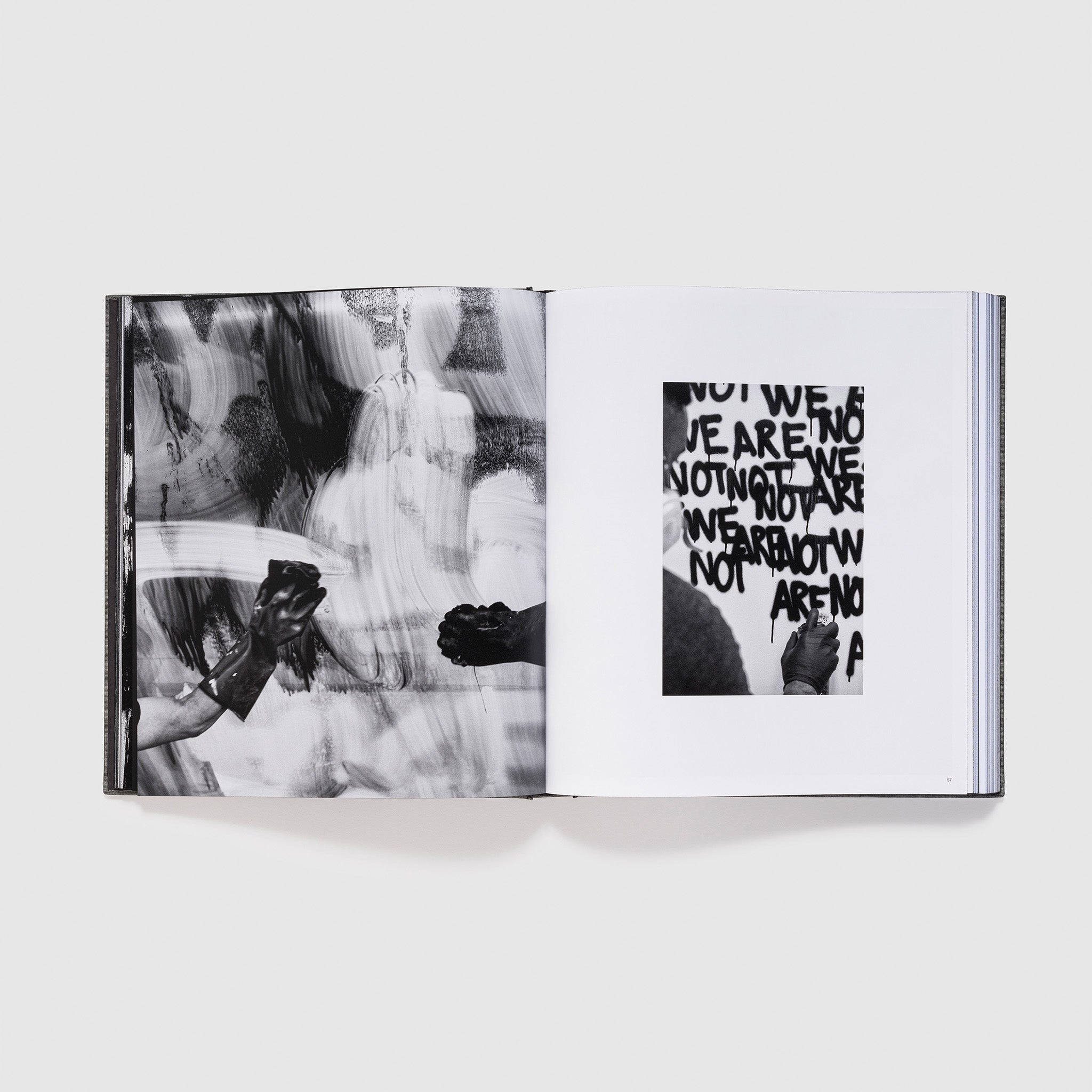 The book is open to two pages. The left page has an image of two hands creating an Adam Pendleton painting. The other page shows Pendleton spray painting a work.