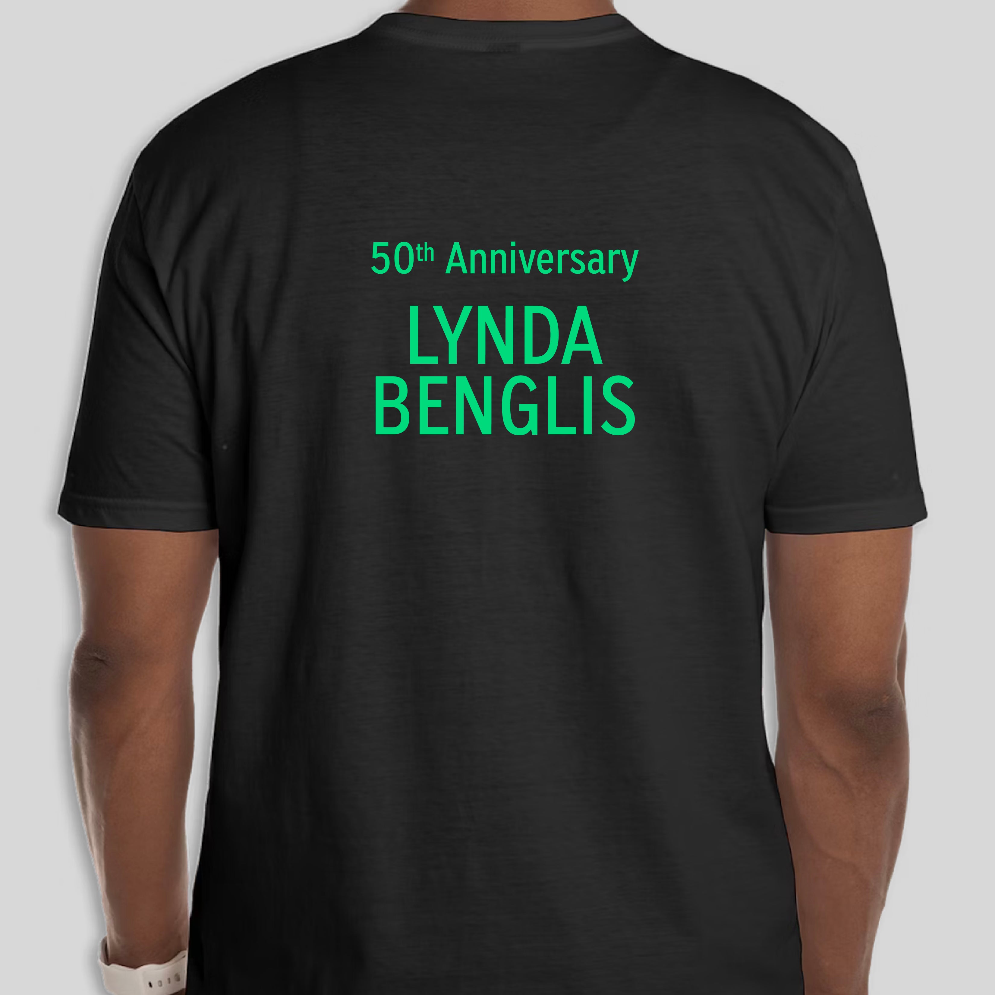 The back of a black tshirt. There are neon green letters that read 50th Anniversary Lynda Benglis.