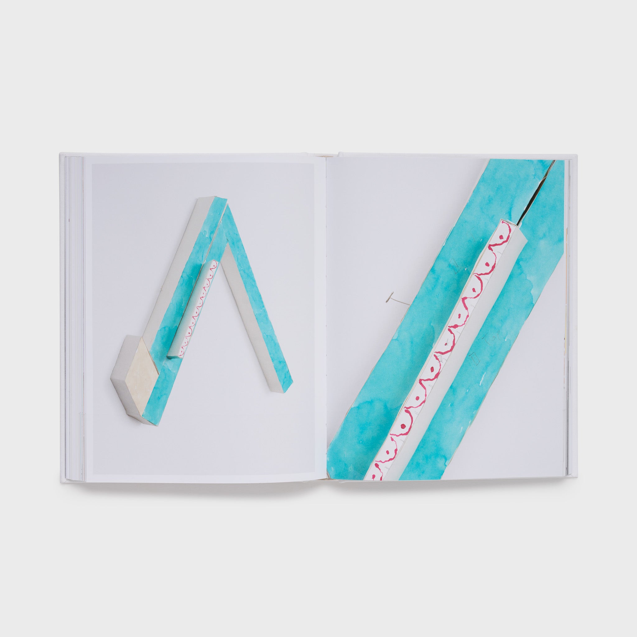 The book is open to two pages with an image of a blue, white, and red Tuttle work on the right page and the same work from a different angle on the left page.