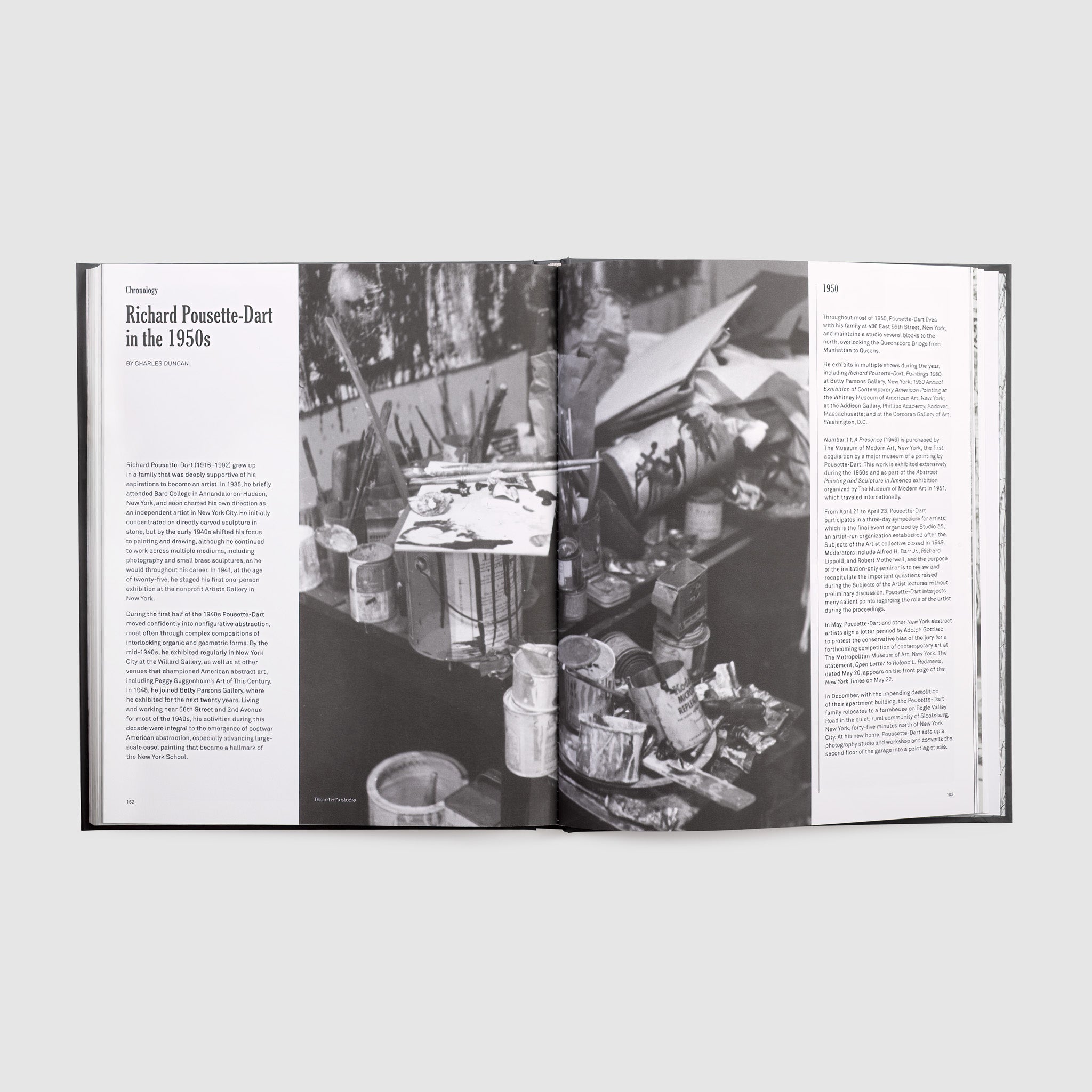 The book is open to two pages. A black and white photo of the artists materials is in the middle of the pages and there&