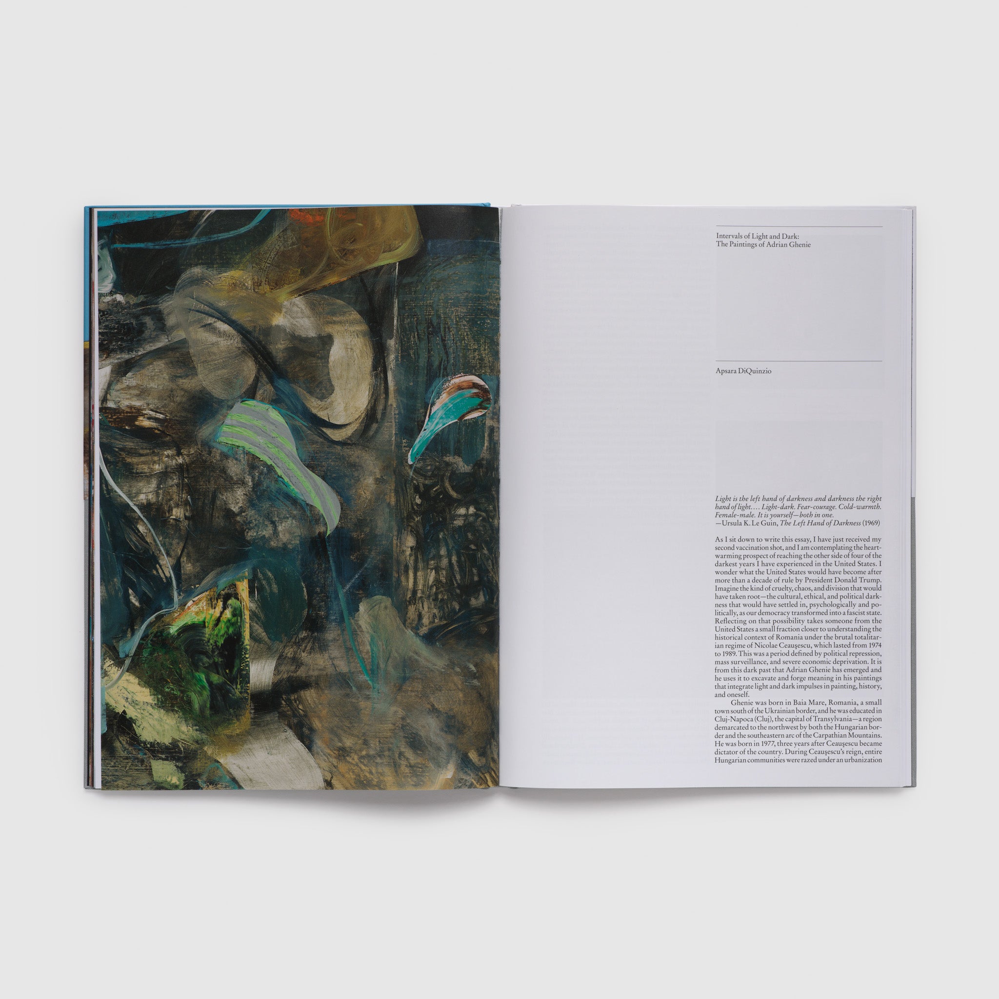 The book is open to two pages with the artists blue, green, and black work on the left page and an essay introduction on the right page.