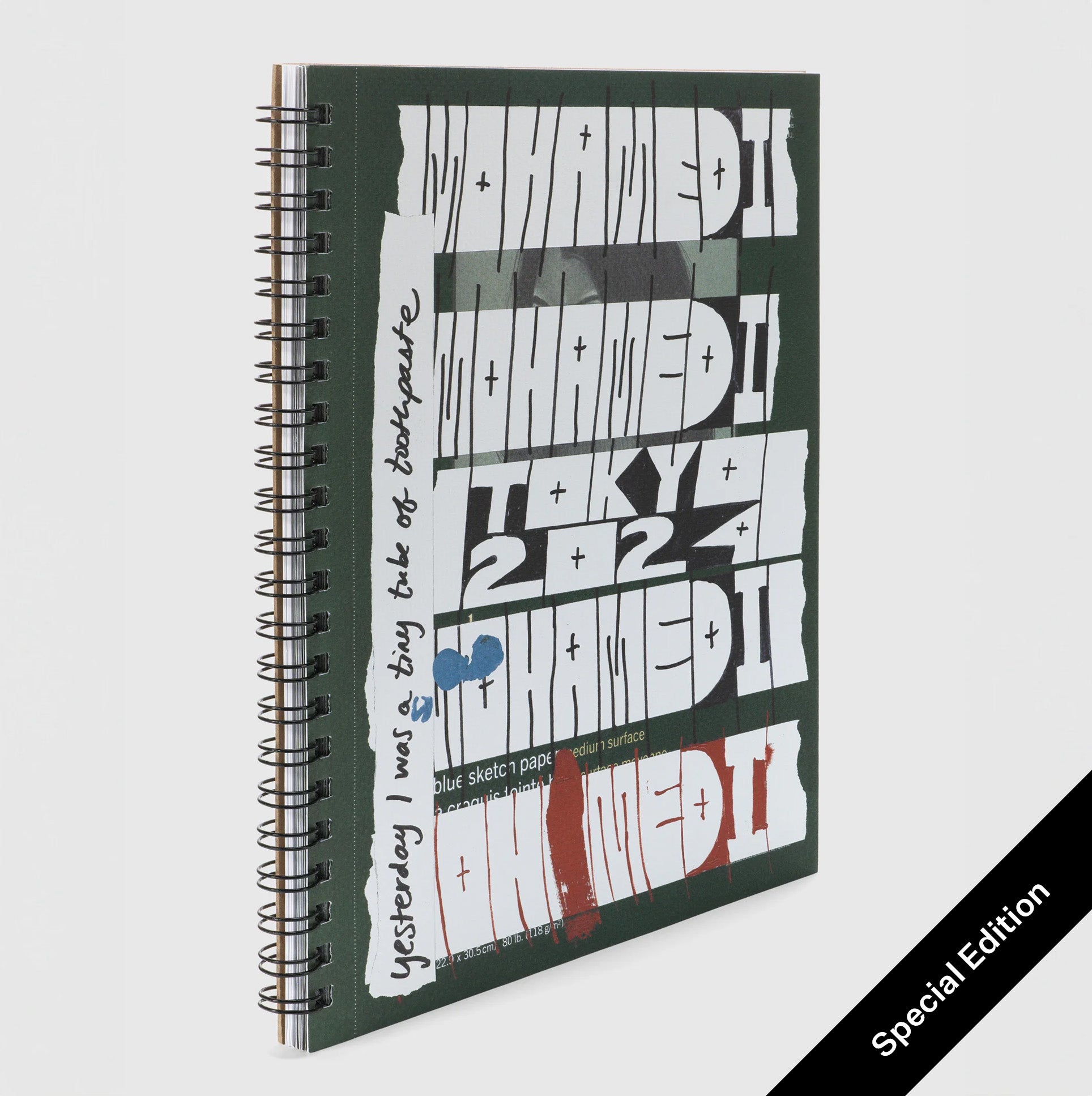 The background of the book cover is dark green and "Mohamedi in Tokyo 2024: yesterday I was a tiny tube of toothpaste" is in white block letters down the front. The book is spiralbound.