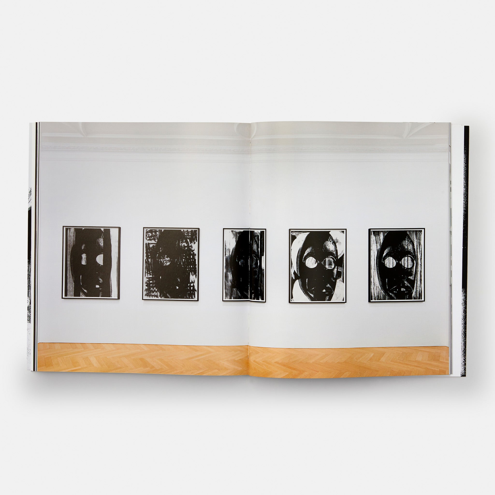The book is open to two pages with one photograph across both that depicts 5 of the artists black and white paintings hanging in a gallery.
