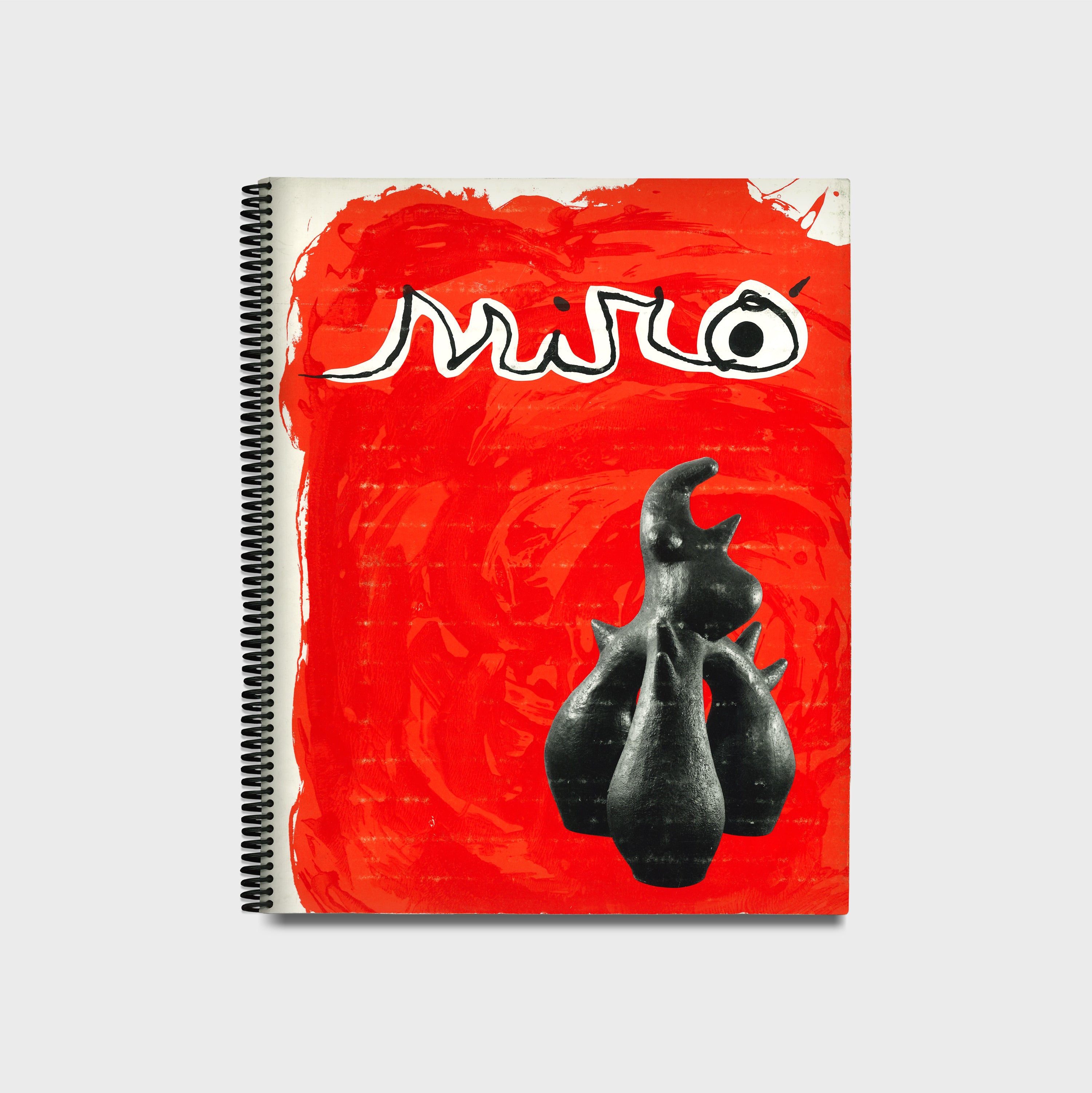 A spiral-bound book with a cardboard cover featuring a red background with the name &