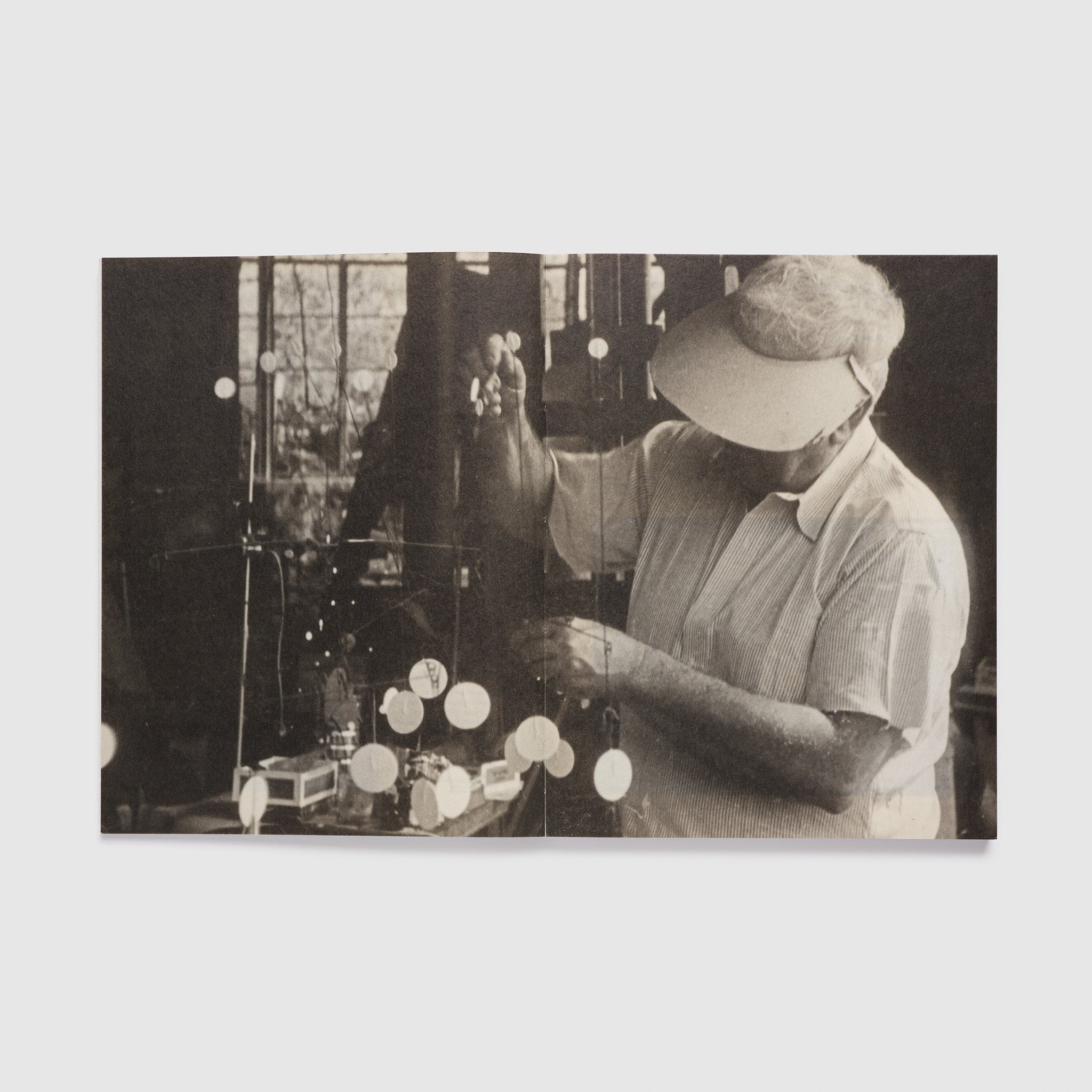 The book is open to two pages with a black and white photo of Calder in his studio across both.