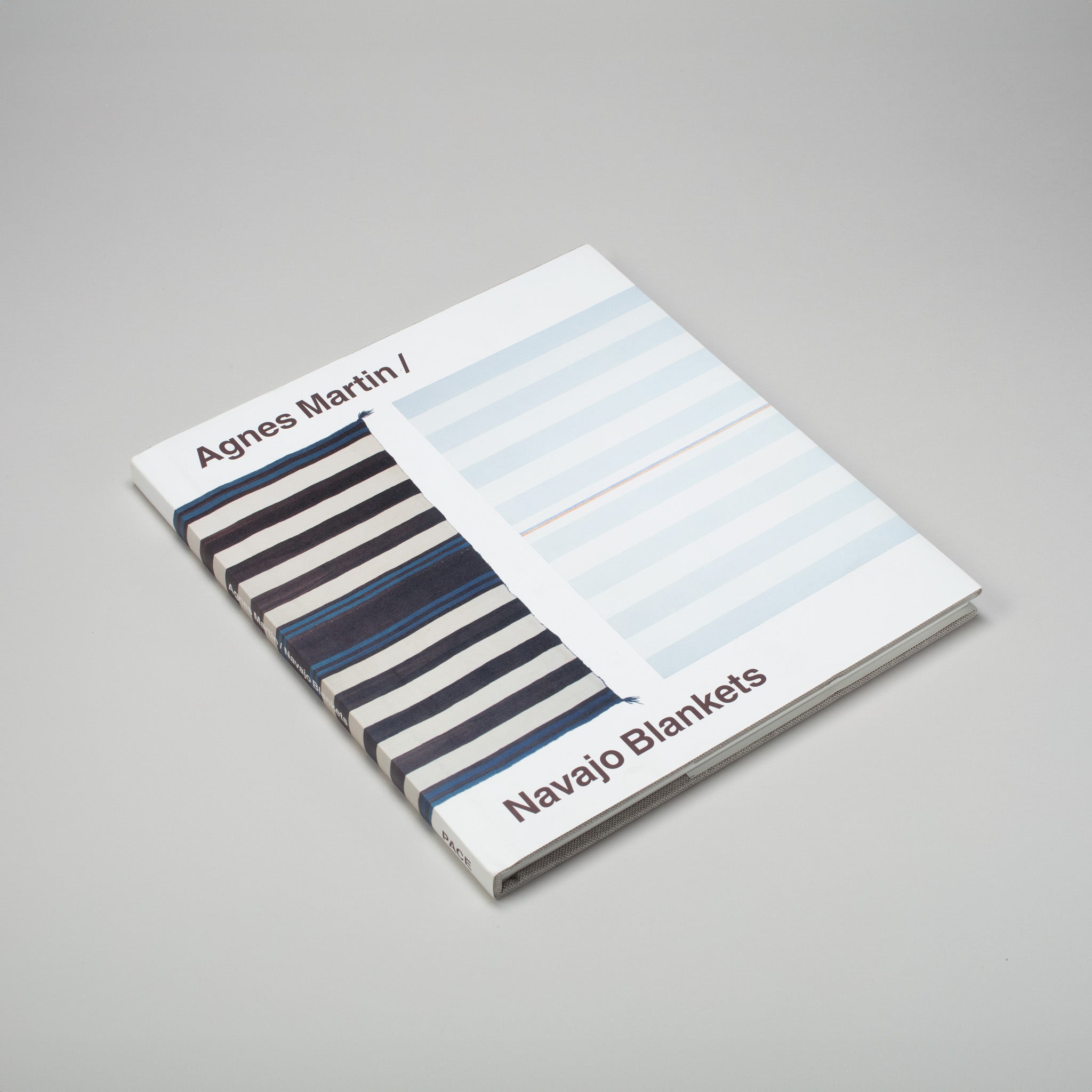 Agnes Martin Navajo Blankets is laying flat on a grey surface. The cover has a blue Navajo blanket next to a blue Agnes Martin painting. 