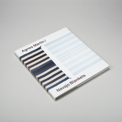 Agnes Martin Navajo Blankets is laying flat on a grey surface. The cover has a blue Navajo blanket next to a blue Agnes Martin painting. 