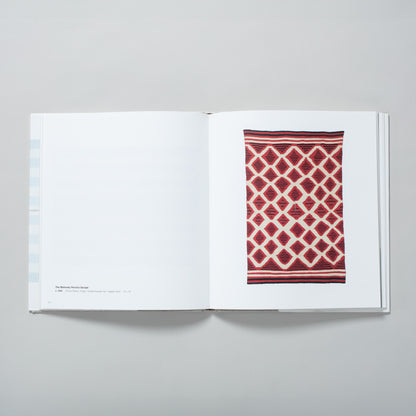 The book is laid flat and open to two pages, on the right page is a red, cream, and black Navajo blanket and the left has black text describing the work.
