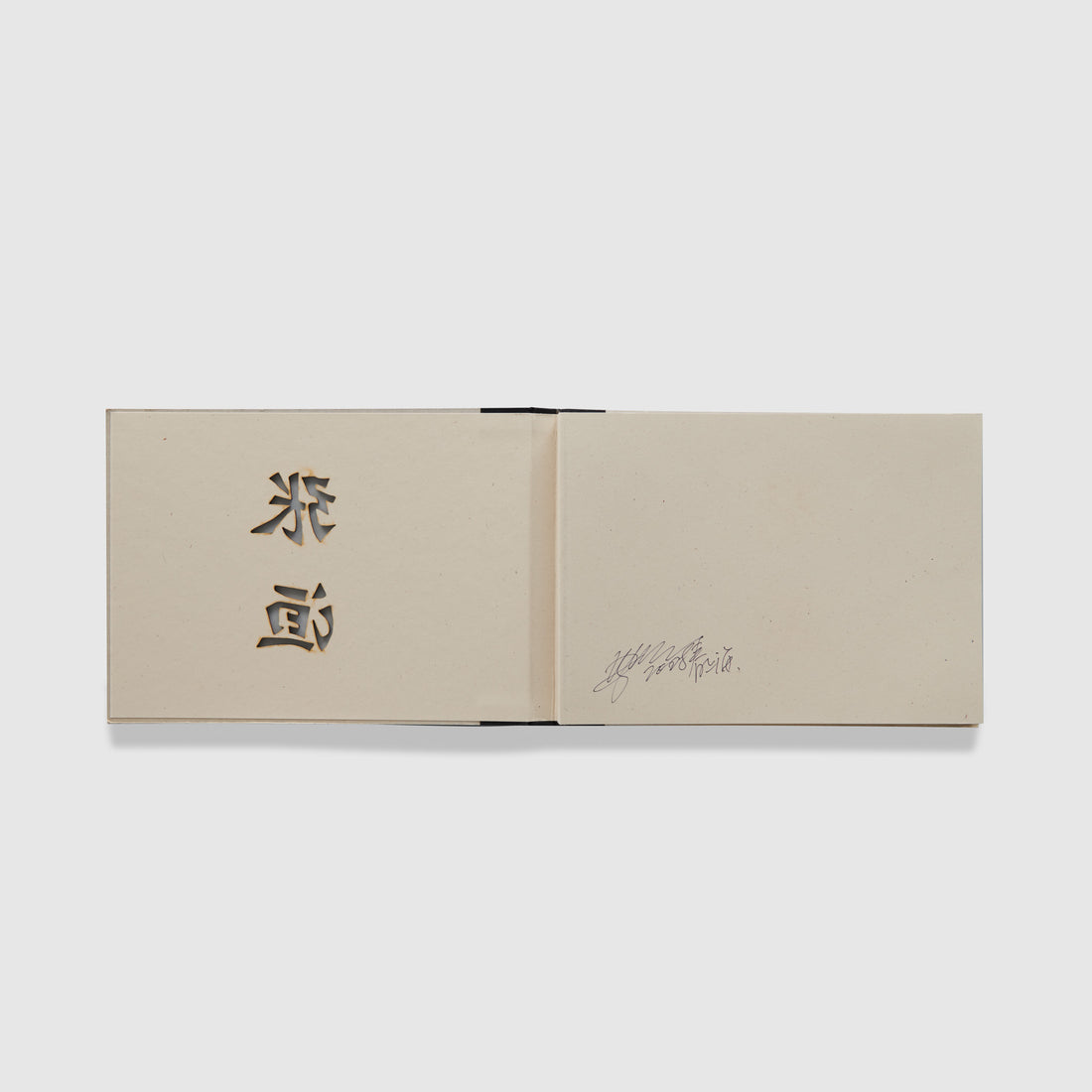 The book is open to two pages. The left page has the cutouts from the cover and the right page has a signature from the artist.